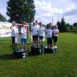 Grupa dzieci ubrana na sportowo na świezym powietrzu stoi na podium z dyplomami.