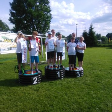 Grupa dzieci ubrana na sportowo stoi na podium z medalami na zewnątrz.