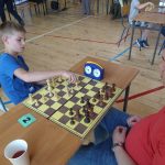 Młody chłopak i starszy mężczyzna grają w szachy na sali gimnastycznej.