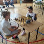 Dziewczynka i chłopiec grają w szachy przy stoliku na sali gimnastycznej.