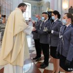 Ksiądz odbierający dary eucharystyczne od czterech funkcjonariuszy policji w kościele.