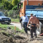 Rozmawiajace osoby. W tle samochody i zieleń.