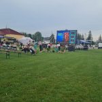 Grupa osób na stadionie, oglądajaca kino w plenerze.,