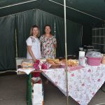 Dwie panie stoją przy stoliku na którym wyłożone są potrawy.