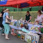 Na stadionie ustawione stoiko z wyrobami rękodzielniczymi. Dwie panie sprzedają a dwie kupują.