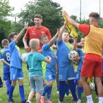 Grupa dzieci w strojach sportowych bierze koszulki do gry w piłkę nożną od zawodników w czerwonych koszulkach.