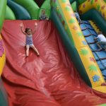 Dziewczynka w ciemnych włosach zjeżdża na dmuchanej zjeżdżalni kolorowej.