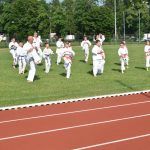 Na trawiastym boisku ćwiczą w strojach uczestnicy pokazu karate.