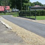 Skrzyżowanie dróg. W tle domy, żywopłot i trawa.