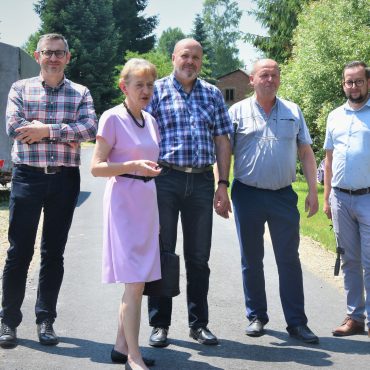 Grupa osób pozujących do zdjęcia. W tle asfaltowa droga i drzewa.