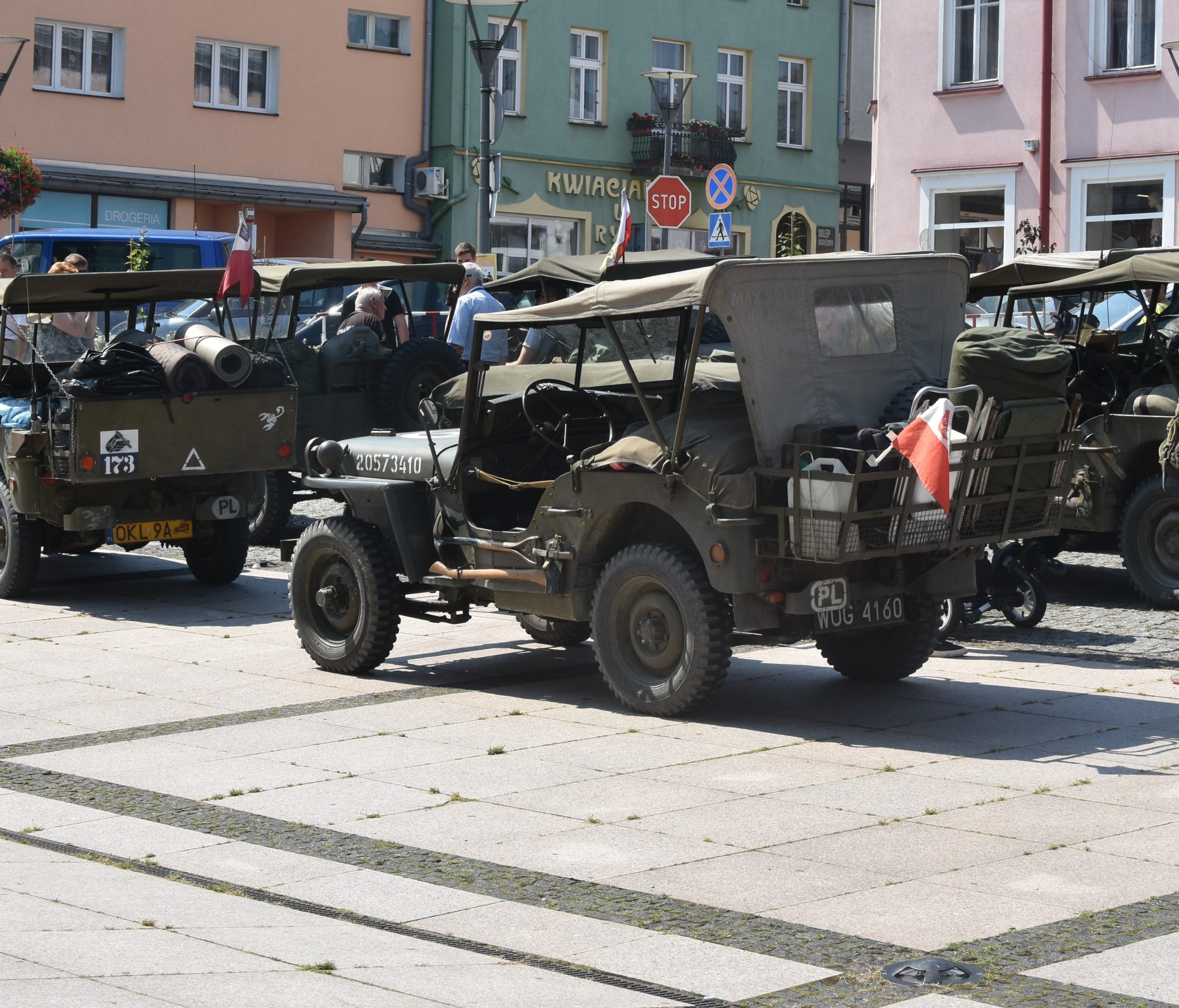 Stare wojskowe samochody na rynku miejskim. W tle zabudowa.