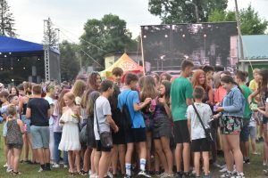 Grupa osób zgromadzona na imprezie. W tle bilbord i namiot.