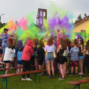 Ciasno stłoczona grupa młodych osób, wyrzucająca w powietrze kolorowe proszki.