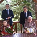 Dwóch stojacych meżczyzn w garniutrów i para staruszków siedząca przy stole.