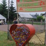 Czerwone, metalowe serce wypełnione zakrętkami. Za nim znajdują się uczestnicy festynu.