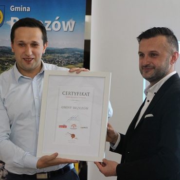 Dwóch mężczyzn pozujących do zdjęcia. Oboje trzyma pamiątkowy certyfikat. W tle rolap.