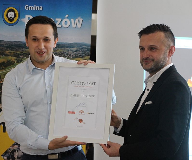 Dwóch mężczyzn pozujących do zdjęcia. Oboje trzyma pamiątkowy certyfikat. W tle rolap.