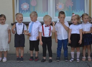 Odświętnie ubrana grupa dzieci, stojąca przed budynkiem.