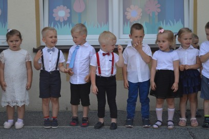 Odświętnie ubrana grupa dzieci, stojąca przed budynkiem.