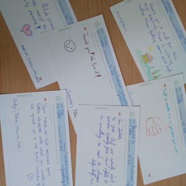 Na drewnianym blacie leżą kartki pocztówki.