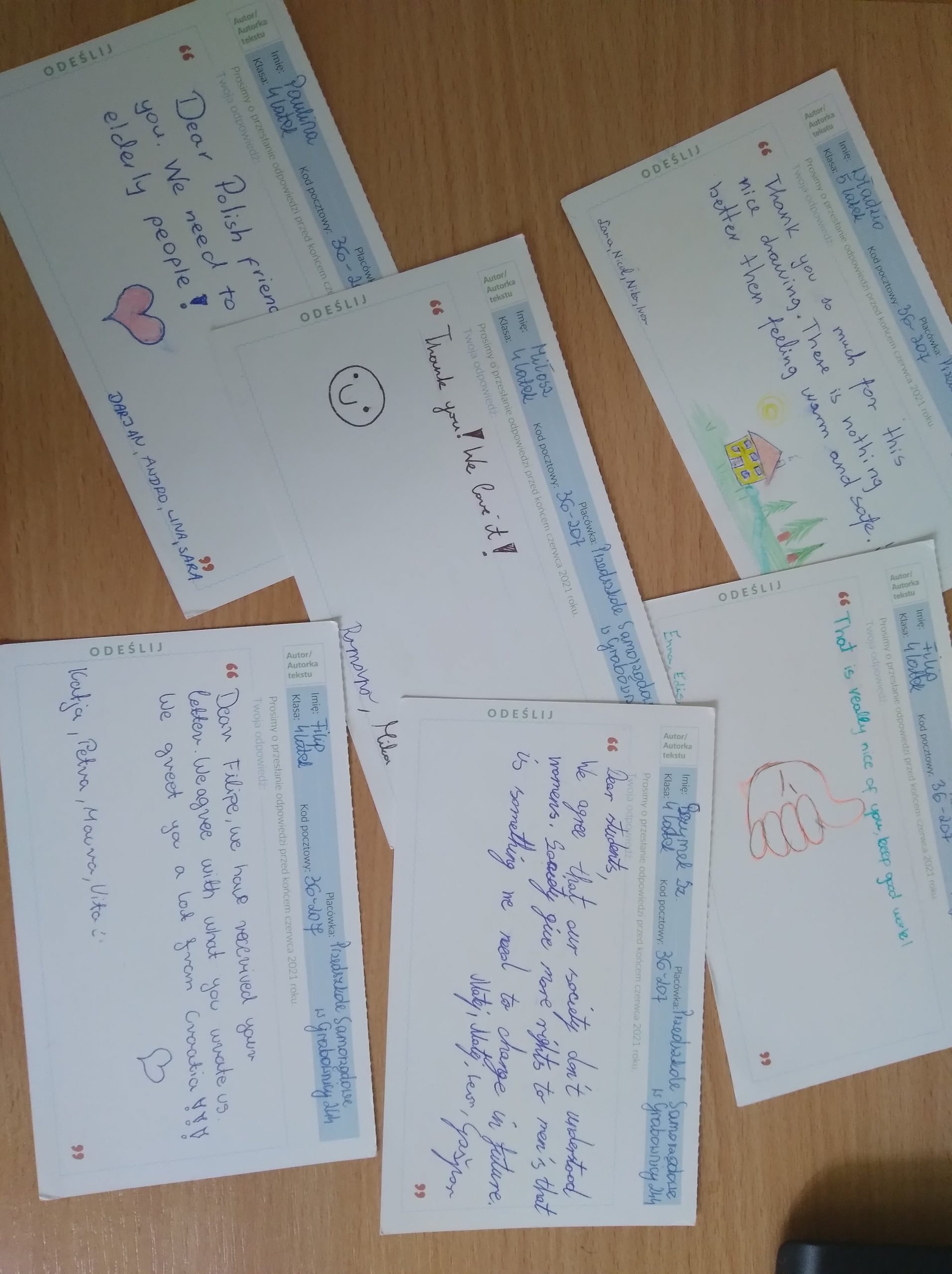 Na drewnianym blacie leżą kartki pocztówki.