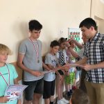 Grupa dzieci stoi przy ścianie i są dekorowanie medalami.