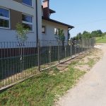 Nowo wybudowane ogrodzenie koło jasnego budynku szkoły.