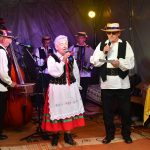 Grupa osób w barwnych strojach ludowych śpiewa pieśni ludowe.