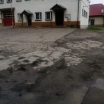 Zniszczony plac asfaltowy przed budynkiem z jasną elewacją.