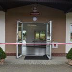 Drzwi do budynku szkoły, przed nimi wisi wstęga biało-czerwona do przecięcia.