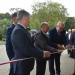 Grupa osób przecina wstęgę przed drzwiami budynku.