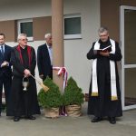 ksiądz święci budynek szkoły przy odświętnie ubranych gościach.