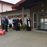 ksiądz święci budynek szkoły przy odświętnie ubranych gościach.