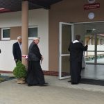 ksiądz święci budynek szkoły przy odświętnie ubranych gościach.