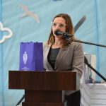 Kobieta w okularach przemawia przy mównicy do mikrofonu na sali gimnastycznej.