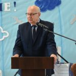 Starszy mężczyzna przemawia do mikrofonu przy mównicy na sali gimnastycznej.