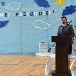 Młoda kobieta w stroju policjanta przemawia do mikrofonu przy mównicy na sali gimnastycznej.