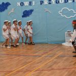 Grupa dzieci w strjach marynarskich na sali gimnastycznej występuje przed widownią.