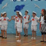 Grupa dzieci w strojach marynarskich wystepuje przed publicznością n a sali gimnastycznej.