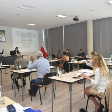 Grupa osób siedzi na sali przy stolikach. Przed nim wyświetlana jest informacja na projektorze.