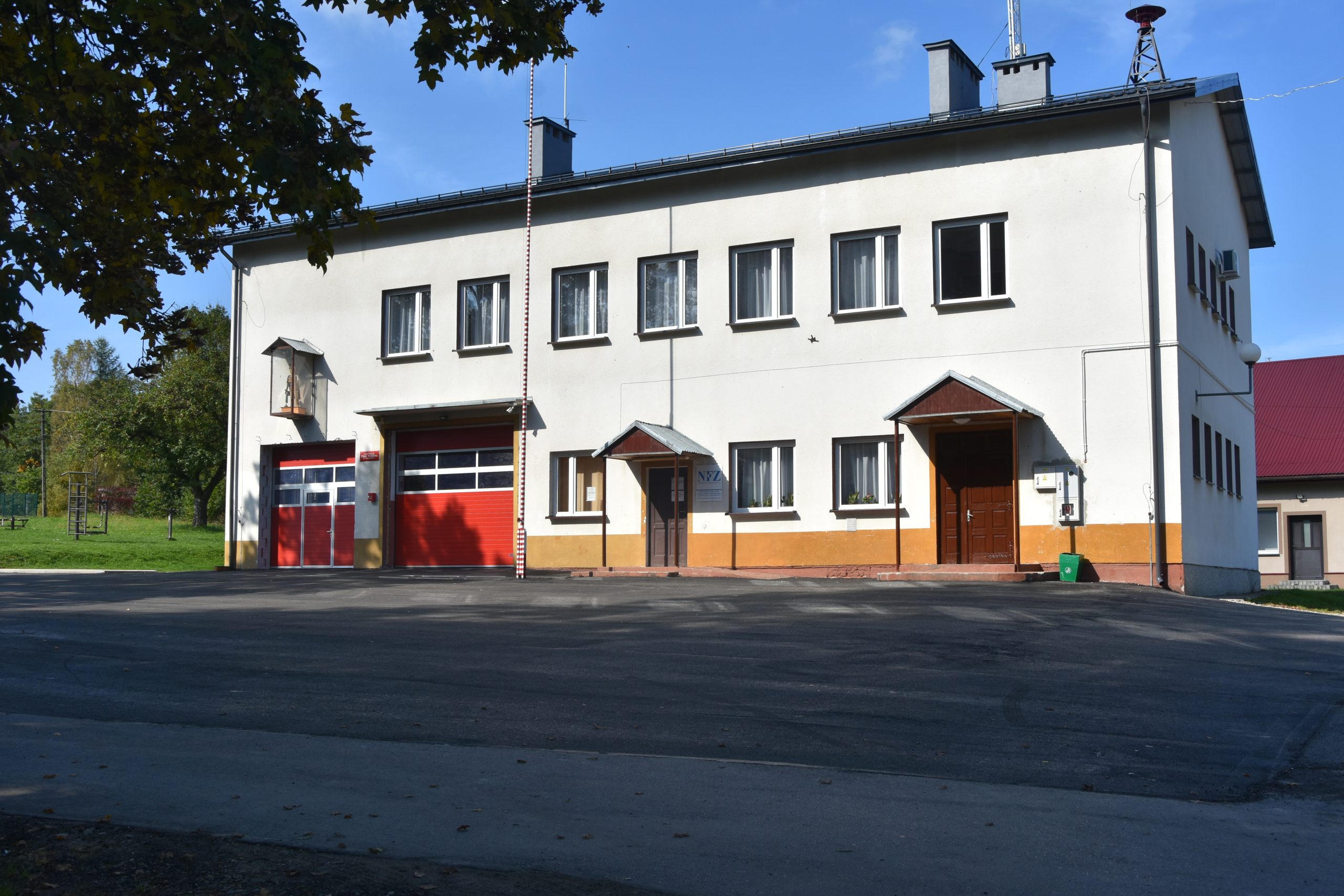 Nowy plac asfaltowy przed budynkiem z jasną elewacją i czerwonymi drzwiami garażowymi.