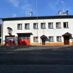 Nowy plac asfaltowy przed budynkiem z jasną elewacją i czerwonymi drzwiami garażowymi.