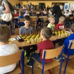 Grupa dzieci gra w szachy przy stolikach w jasnym pomieszczeniu sali gimnastycznej .