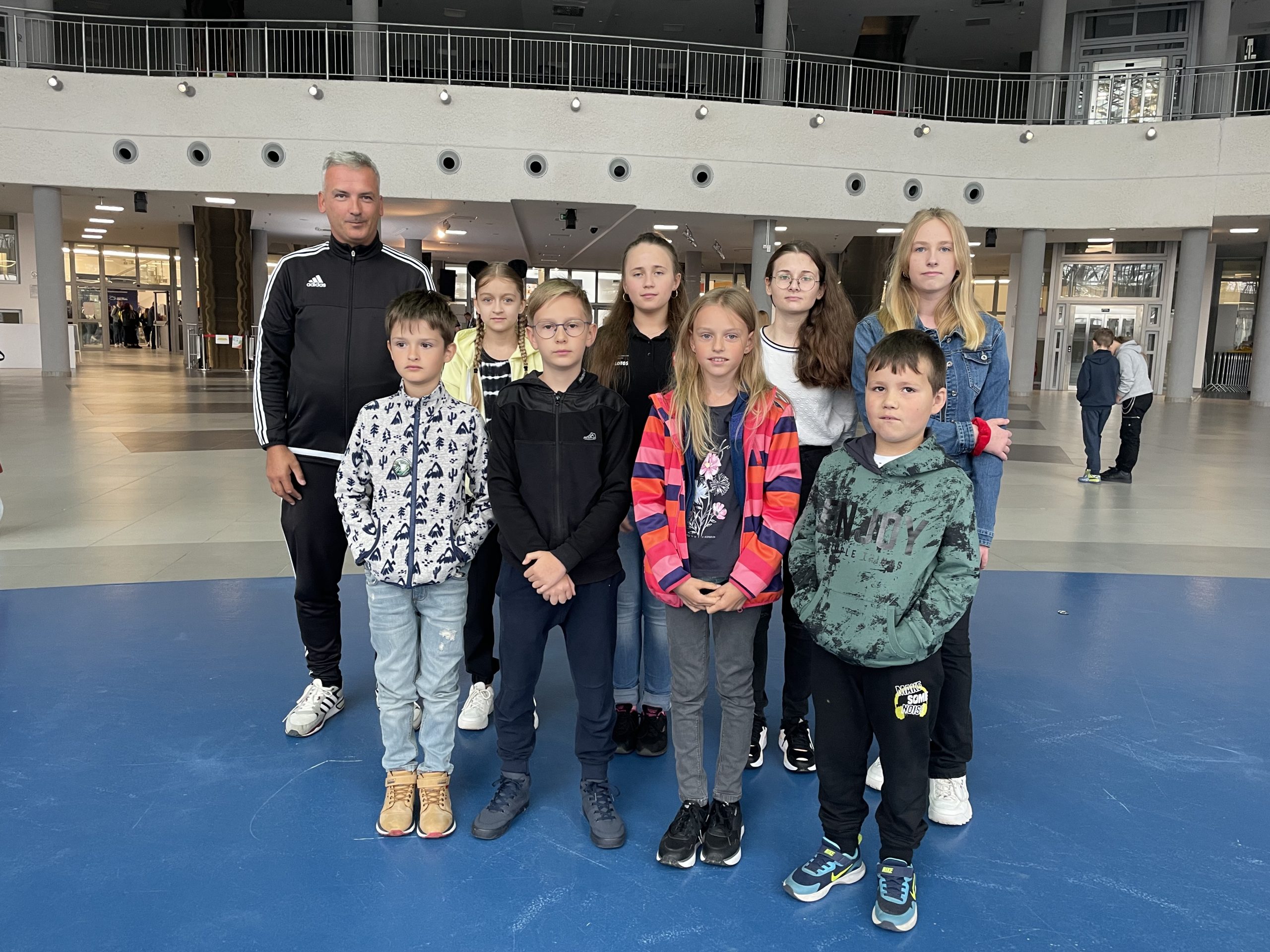 Grupa dzieci stoi w dużym pomieszczeniu konferencyjnym.