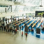 Duża jasna sala konferencyjna , na środku hali stoją stoły, a na nich rozstawione szachy. Na sali przebywa kilkaset osób.