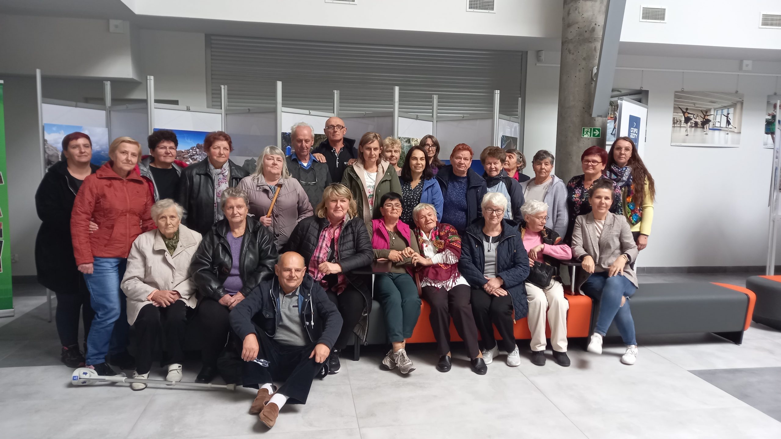 Grupa ludzi z SLT Brzozów pozują wspólnie do zdjęcia z grupą z puław. Znajdują się w budynku z białymi ścianami i siedzą na sofie