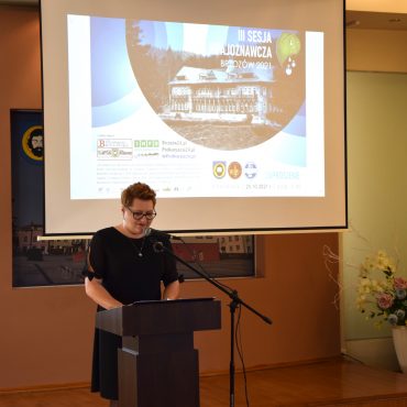 Kobieta ubrana na czarno stojąca przy mównicy wita gości