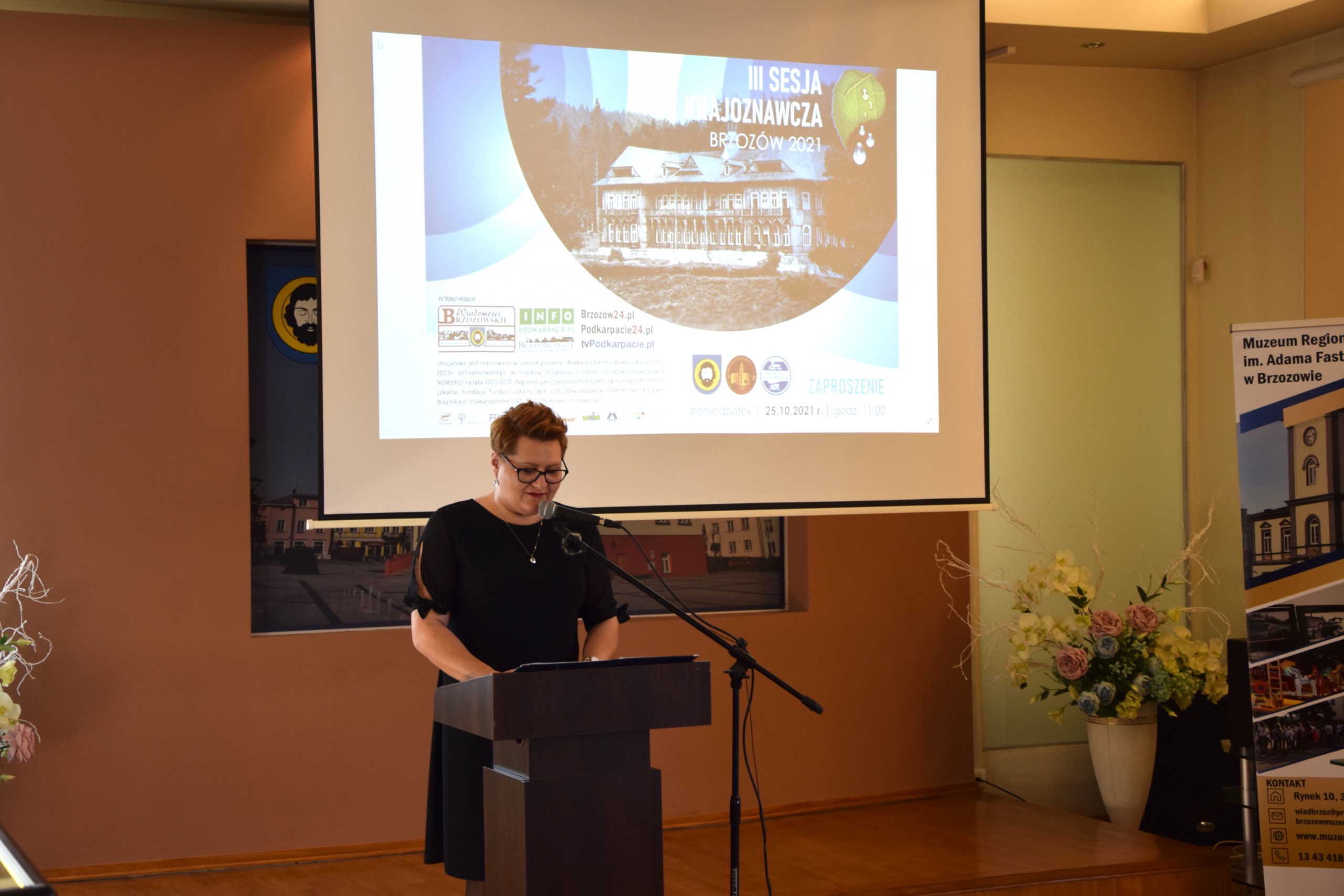 Kobieta ubrana na czarno stojąca przy mównicy wita gości