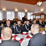 Druhowie i druhny siedzą przy zastawionym stole ubrani w mundury galowe.