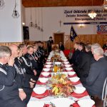 Druhowie i druhny siedzą przy zastawionym stole ubrani w mundury galowe.